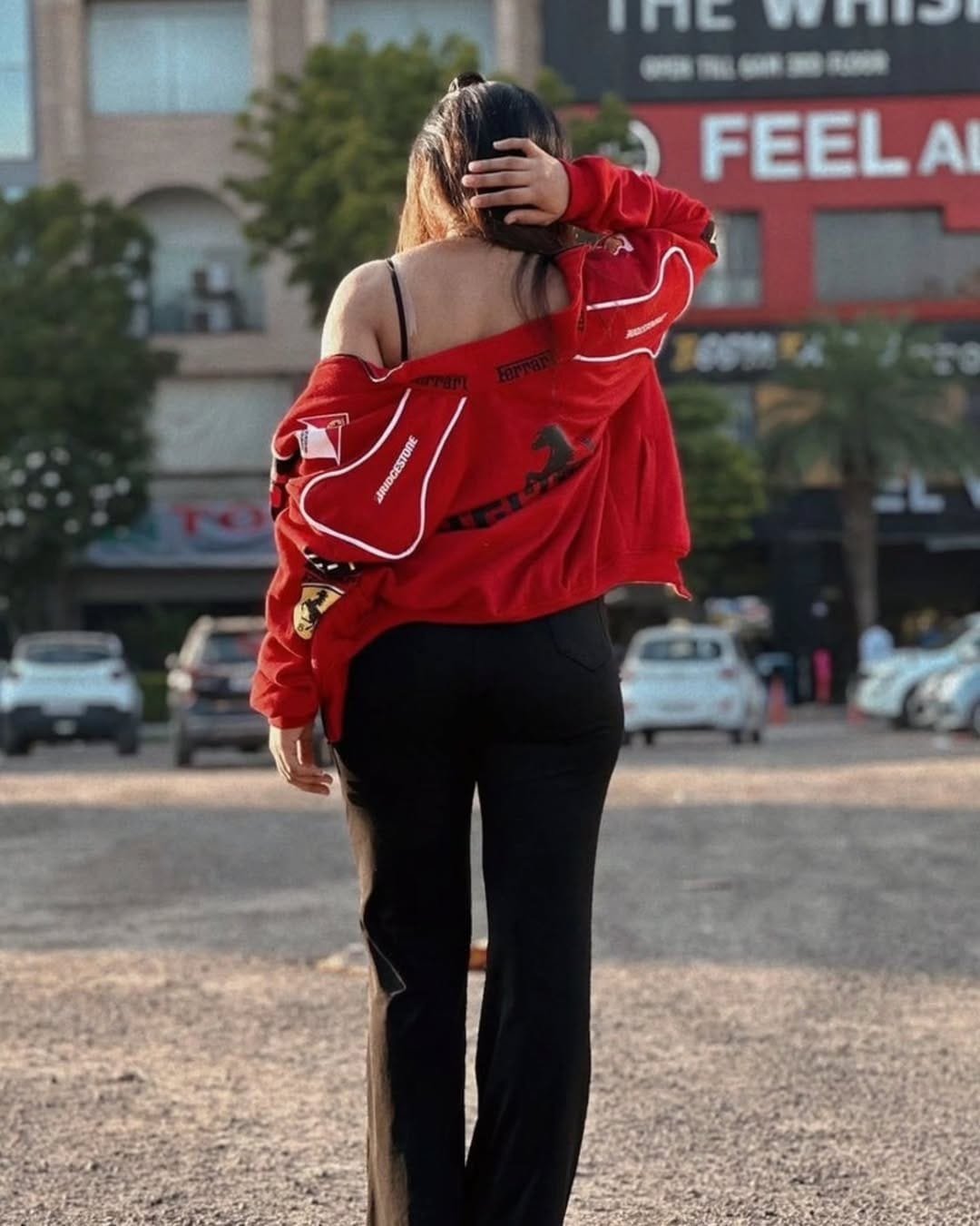 Woman wearing a red Ferrari jacket unisex style with black pants, showcasing streetwear-inspired motorsport apparel outdoors.